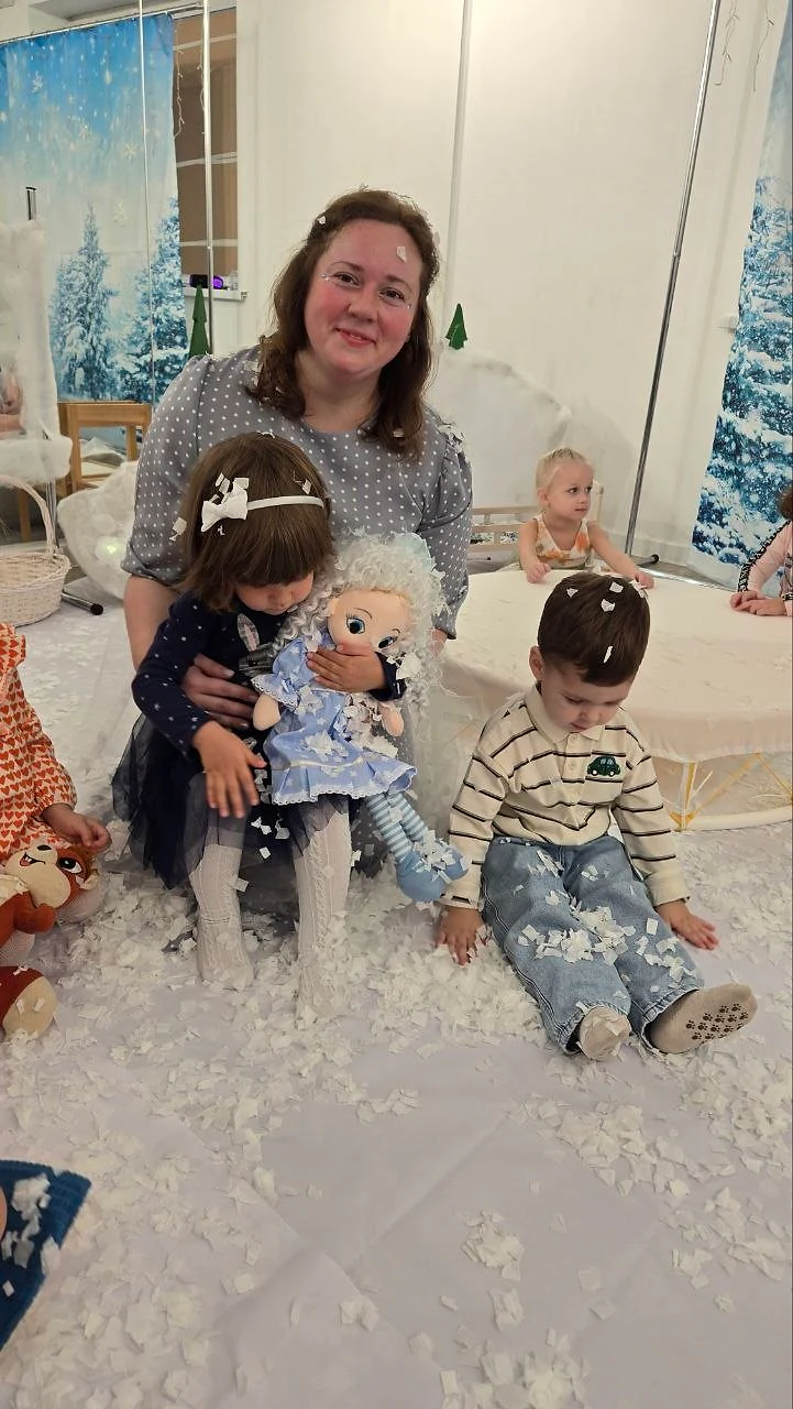 Педагог и дети играют с куклой среди мягкого снега
